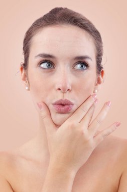 Kameraya öpücük yollayan bir kadın yüzüne dokunurken yana doğru bakıyor doğal cilt, sivilce ve sivilceler gösteriyor. Cilt bakımından önce otantik bir kadın portresi. Bej rengi ile izole edilmiş.