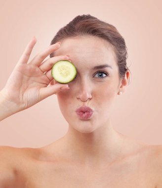 Bir kadın gözlerini salatalık dilimleriyle kapayıp öpüşürken doğal cildini sivilceli ve lekeli gösterir. Cilt bakımı öncesi özgün portre ya da yaşlanmayı önleyen güzellik tedavisi. Bej rengi ile izole edilmiş.