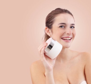 Makyajlı gülümseyen genç bir kadın yüzüne plastik bir makyaj kremi tutuyordu. Cilt bakımı ve güzellik tedavisi rutin konsepti. Bej arkaplanda izole edilmiş