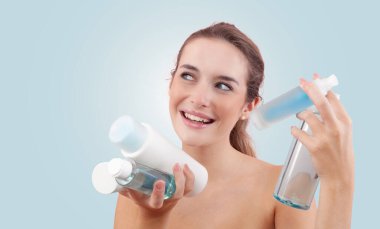 Elinde mikiler suyu ve duş jeli de dahil olmak üzere çeşitli cilt bakımı şişeleri ve banyo ürünleri tutan gülümseyen genç bir kadın. Günlük güzellik, temiz cilt ve hijyen konsepti. Mavi arkaplanda izole