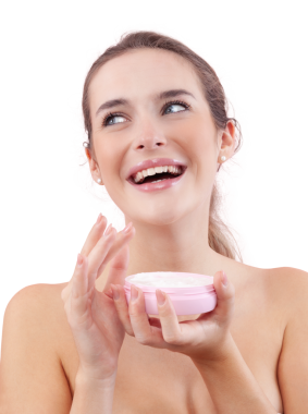 Makyajlı gülümseyen genç bir kadın yan bakarken yüzünde açık plastik bir yüz kremi kavanozu tutuyor. Cilt bakımı ve güzellik tedavisi rutin konsepti. Beyaz arkaplanda izole