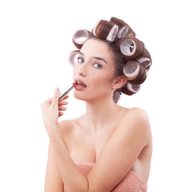 Makyaj, mavi gözleriyle kameraya bakarken saç bigudiyle ruj süren gülümseyen genç kadın. Saç stili, makyaj, güzellik ve kozmetik anlayışı. Beyazda izole edilmiş