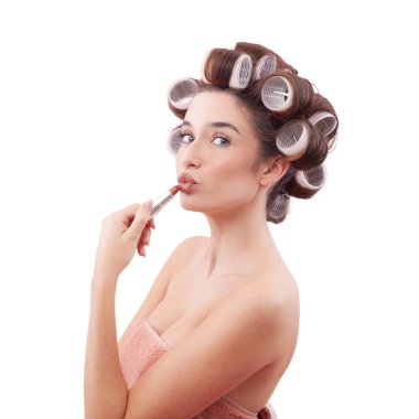 Makyaj, saç bigudili genç bir kadın öpücük dudaklarına ruj sürüp mavi gözleriyle kameraya bakıyor. Saç stili, makyaj, güzellik ve kozmetik anlayışı. Beyazda izole edilmiş.