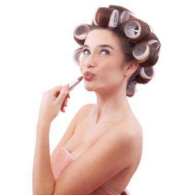 Makyaj, saç bigudili genç bir kadın öpüşürken dudaklarına ruj sürüp mavi gözleriyle yan tarafa bakıyor. Saç stili, makyaj, güzellik ve kozmetik anlayışı. Beyazda izole edilmiş.