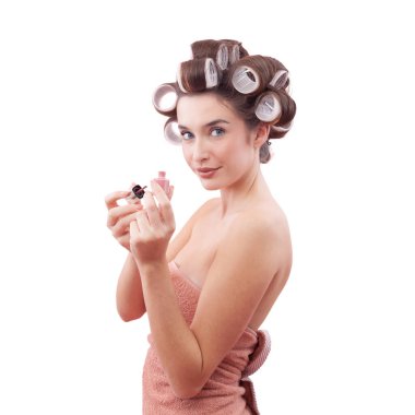 Mavi gözleriyle kameraya bakarken tırnak cilası süren saç bigudiyle gülümseyen genç bir kadın. Saç stili, makyaj, güzellik ve kozmetik anlayışı. Beyaz arkaplanda izole