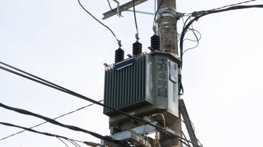 Beton bir elektrik direğine monte edilmiş elektrik transformatörünün detaylı bir görüntüsü, temiz bir gökyüzüne karşı karmaşık elektrik hatlarıyla çevrili..