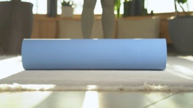 Çalışmaya başlamak için genç bir bayanı spor minderini açmaya hazırla. Güzel ışıkta yoga pratiğini rahatlatmak için mavi hasırı hazırlıyorum. Sağlıklı ve formda kalmak için spor egzersizine hazırlanıyorum.