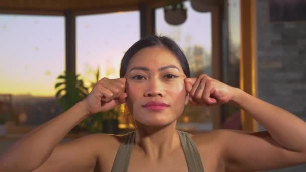 漂亮的亚洲女人自我按摩 放松面部肌肉 面部瑜伽练习使面部放松 美丽的女性在金色的光芒下触摸和自我按摩她的脸 — 图库视频影像