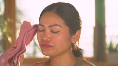 Sportif Asyalı kadın yoğun idmandan sonra yüzünden ter siliyor. Genç bir bayan fiziksel egzersizden sonra terini silmek için pembe havlu kullanıyor. Ev sporu etkinliği sırasında ara veriyoruz..