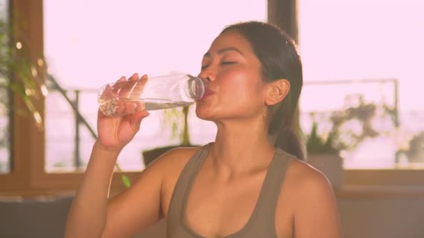 漂亮的亚洲女人在剧烈运动后从瓶子里喝水 在家庭体育活动中休息一下的年轻女性 喝清水解渴 — 图库视频影像