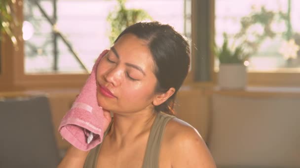 经过密集训练后 漂亮的亚洲女人正在擦拭脸上的汗珠 年轻女子运动后用粉红毛巾擦汗 在家庭体育活动中休息 — 图库视频影像