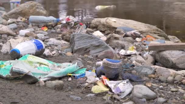 閉じる 廃棄物管理の問題として 川の銀行で洪水プラスチックごみやその他のゴミ 砂の川の海岸に川の破片やプラスチックごみの混合物 環境意識を高める必要性 — ストック動画