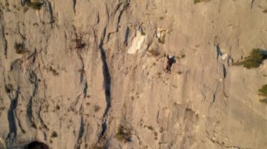 Kaya tırmanışçısı, güneş ışığıyla aydınlanan kireçtaşı duvarına tırmanan bir iple donatılmış. Duvara tırmanan ve iyi tutuş arayan bir adam. Güzel doğal çevrede adrenalin aktivitesi..