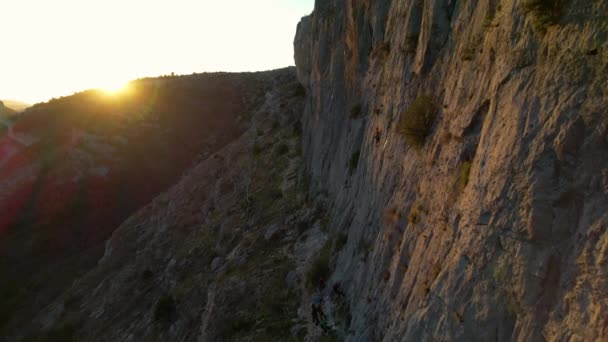 Aerial 女性登山家が背景に金色の太陽のフレアで壁を登る 日没時には壁の真ん中に女性登山 美しい自然環境の中でアドレナリン屋外活動 — ストック動画