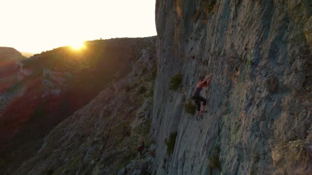 Aerial 女性は背景に金色の太陽のフレアで石灰岩の壁を登る 女性登山者が壁を登り 良いグリップを探します 美しい自然環境の中で屋外活動 — ストック動画