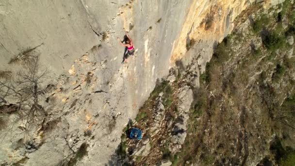 スポーティ若い女性はロープを取り付けるために登山をリードし クイックドローを使用しています 石灰岩の壁を登るの真ん中に女性のロッククライマー 美しい屋外環境でアドレナリンスポーツ活動 — ストック動画