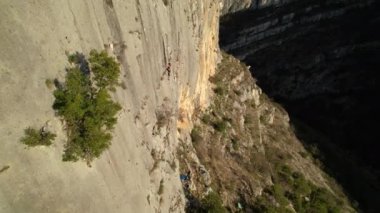 Güneş ışığıyla aydınlanan duvara yakın uçmak ve kadın kaya tırmanışçısına yaklaşmak. Güzel ve pitoresk bir çevrede adrenalin aktivitesi. Sportif genç kadın kaya duvarına tırmanıyor..