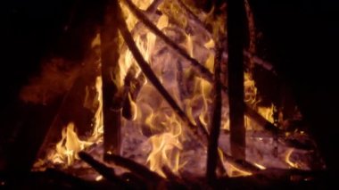 Alevli odun parçaları şenlik ateşinde ve yanan közlerde yığıldı. Siyah arka planda yanan odunların yüksek kontrastlı görüntüsü. Ahşap kalıntıların etrafında dönen alev ve duman..