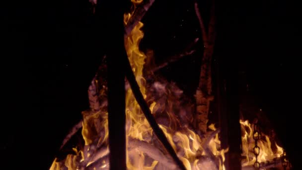 スローモーション 輝くメンバーからのたき火の眺め 炎の木と飛んで火花 黒い背景に対する火照りのログの表示とは対照的です 薪の周りに火と煙が残っている — ストック動画