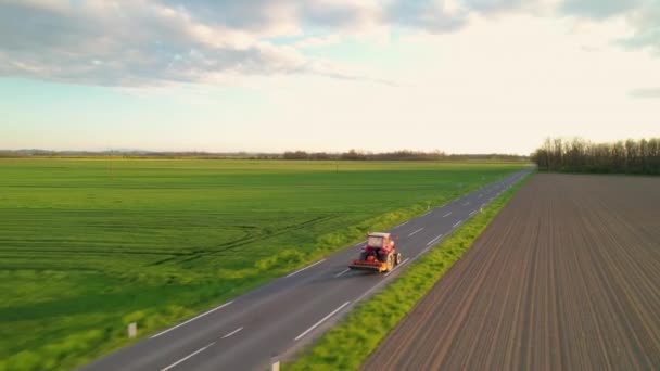 Aerial 田舎道を走行する付属の農業機器を備えた赤いトラクター 農業分野を維持することからトラクターで帰国作業農家 重農作業用の近代的な機械 — ストック動画