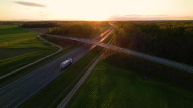 Kırsal bir otoyol ve yol üst geçidinde altın güneş ışığı altında düşük trafik. Otoyolda giden kamyonlar ve arabalar. Orman ağaçlarıyla dolu güzel yeşil arazide seyahat eden araçlar..