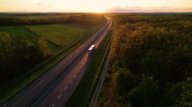 Güzel altın ışıkta kırsal bir otoyolda kargo kamyonları konvoyu. Muhteşem bir ışıkla güzel manzarayı geçen bir otoyolda düşük trafik. Mal teslimatı için kamyon taşımacılığı.
