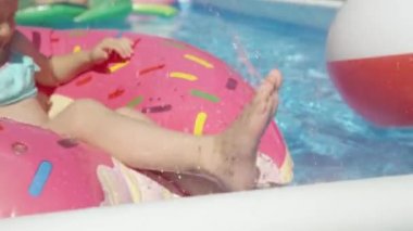Yüzme havuzunda yüzen donuttan su sıçrayan bebek bacakları. Küçük kız havuz partisinde eğlenirken su sıçratıyor. Arka bahçede sıcak günler için yaz tatili aktiviteleri