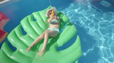 Su tabancasıyla kameraya doğru püskürtülen bir şamandıranın üzerinde uzanan oyuncu kız. Neşeli küçük kız yüzme havuzunda yüzüyor ve kameraya püskürtülmüş su tabancasıyla eğleniyor.