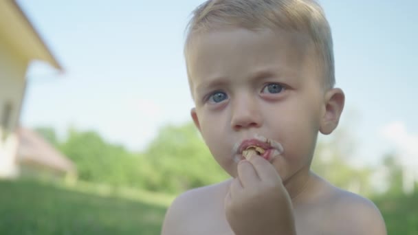 夏天的一天 小男孩在花园的阴影下吃完了他的冰淇淋 可爱的蹒跚学步的幼儿在后院阴凉的地方享受香草冰淇淋锥 在炎热阳光灿烂的夏日里好好地放松一下 — 图库视频影像