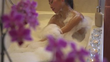 Genç ve güzel bir bayan kendini köpükle yıkıyor ve dinleniyor. Güzel Filipinli kadın ev banyosunda spa tedavisinin keyfini çıkarırken rahatlatıcı bir atmosferde köpüklü banyo yapıyor..