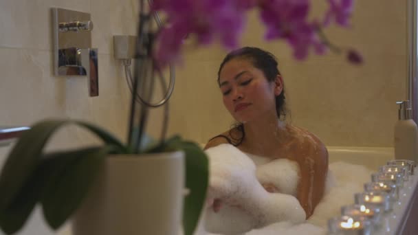 リラックスした雰囲気の中で泡風呂を楽しむ美しい若いアジアの女性 1日の終わりのための家庭用バスルームでのリラクゼーションとスパトリートメント 女は泡風呂で自分自身を治療 — ストック動画