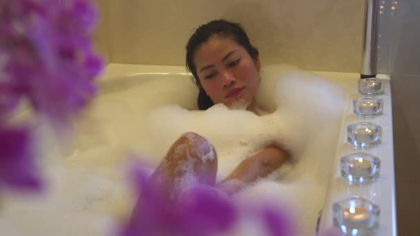 漂亮的菲律宾女人一边洗澡一边享受着泡泡浴 年轻的女性躺在充满泡沫的浴池中 凝视着相机 放松下来 家居浴室的美容疗法 — 图库视频影像