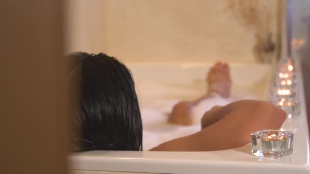揭示了年轻女子在泡泡浴中放松并扭动着脚的镜头 女性在充满泡沫的浴缸里冷冰冰地享受着 四周点满了蜡烛 漫长而忙碌的一天之后的放松 — 图库视频影像