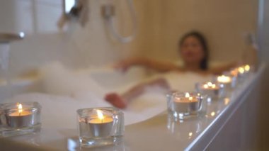 Güzel bir köpük banyosu yaparken atmosferi rahatlatmak için mum dizdim. Güzel, genç Asyalı bir kadın, köpüklü bir küvette dinlenirken kendine spa ve rahatlama hizmeti veriyor..