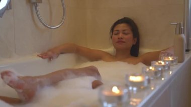 Gözleri kapalı rahat bir kadın mumlarla çevrili köpüklü bir banyonun tadını çıkarıyor. Ev banyosunda spa tedavisi görürken rahatlatıcı atmosfer ve hoş bir deneyim için parlak mumlar dizdim..