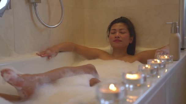 一个松懈的女人闭上双眼 享受着充满蜡烛的泡泡浴 在家里的浴室里 在温泉疗养过程中 点燃了点燃的蜡烛 营造了轻松的氛围和愉快的体验 — 图库视频影像