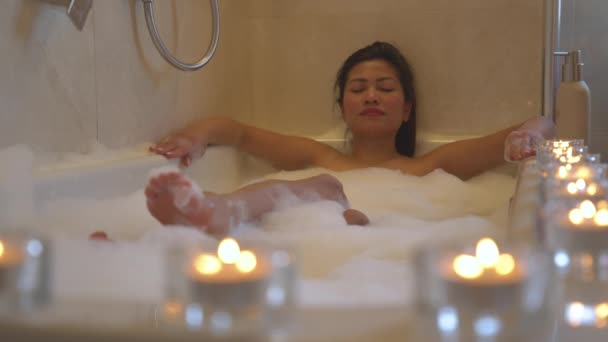 迷人的女士 眼睛闭着 在泡着蜡烛的泡泡浴中 冷冰冰的 年轻的亚洲女人在浴缸里放松 点上点燃的蜡烛 营造轻松的氛围和愉快的温泉体验 — 图库视频影像