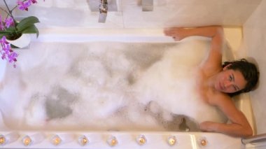 Mumlarla çevrili lüks köpük banyosunun keyfini çıkaran güzel bir kadın. Çekici Filipinli kadın, parlak mumlar ve mor orkide çiçeğiyle rahatlatıcı atmosferde spa tedavisi görüyor.