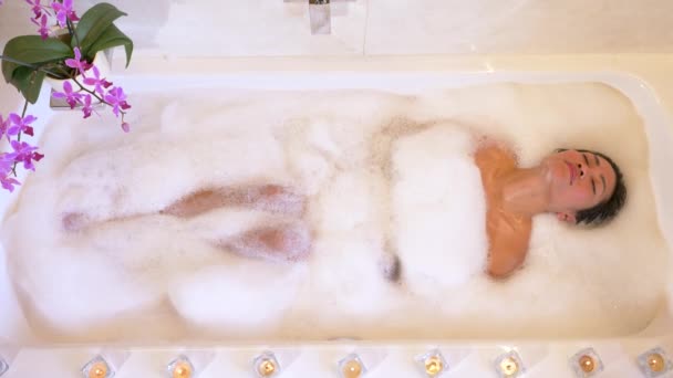 可爱的亚洲女人在泡满泡沫的浴池中尽情享受 在浴池边缘点燃蜡烛 在享受健康治疗的同时 舒缓气氛和愉快的体验 — 图库视频影像