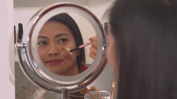閉じる 彼女の顔を美化するために粉末ブロンザーを適用魅力的な若いアジアの女性 顔の赤面を適用するためにブラシを使用してきれいな女性のミラー反射 彼女の新鮮な表情を世話する女性の人 — ストック動画