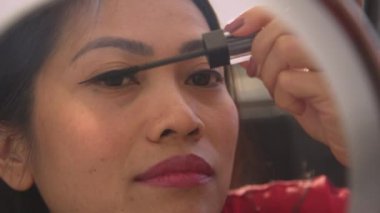 Filipinli güzel bir kadının kirpiklerine rimel sürerken detaylı görüntüsü. Genç bayan aynanın karşısında özel bir durum için makyaj yapıyor. Görünüşüne dikkat eden bir kadın..