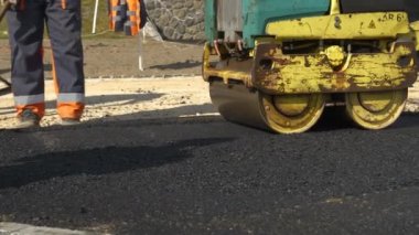 Garaj yolunu asfaltlarken asfalt silindirle çalışan bir işçi. Sıkıştırma ve pürüzsüz yüzey için makine kullanılıyor. Üniformalı asfalt giymiş adamlar güzel bir sabah ışığında bahçeyi asfaltlıyorlar..