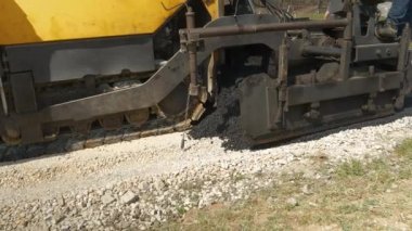 Asfalt kaldırım taşı makinesi ezilmiş kayaların üzerine dökülüp asfalt yayıyor. İnşaat işçileri, sabah vakti garaj yolunda siyah asfalt yüzeyi döşemek için ağır makinelerle çalışıyorlar..
