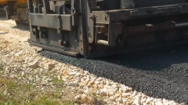 Arkadan ağır asfalt kaldırım taşı makinesinin taze asfalt bırakması. İnşaat işçileri, sabah vakti otoparkta siyah asfalt yüzeyi oluşturmak için ağır makinelerle çalışıyorlar..