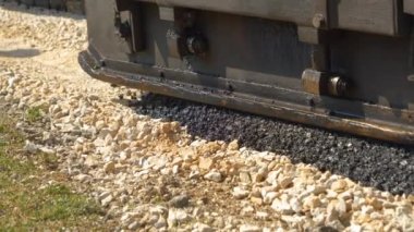 Ezilmiş kayaların üzerine asfalt kaldırım makinesiyle siyah asfalt sermek. Güzel bir sabah ışığında otoparkta ağır inşaat makinelerinin boşaltımını ve taze asfalt yüzeyi görüntüsü..