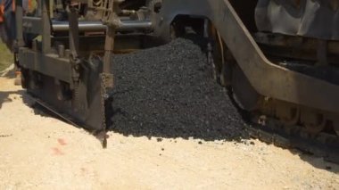 İşçi, asfalt kaldırım makinesi tarafından atılan bir kürek taze asfalt alır. İnşaat işçileri, sabah vakti otoparkta siyah asfalt yüzeyi oluşturmak için ağır makinelerle çalışıyorlar..