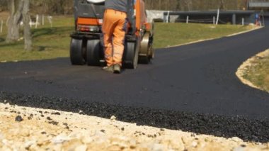 Yol işçileri yeni asfalt zemini döşeyip düzleştiriyor. İnşaat işçileri asfalt silindirlerini ve hurdacıları kullanarak sabah güneşinde asfalt yola son rötuşlarını yapıyorlar..