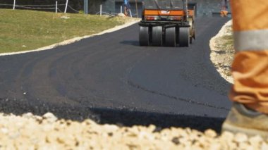 Asfalt paten sıkışıyor ve yeni yerleştirilmiş asfalt yüzeyini dümdüz ediyor. İnşaat makinelerini çalıştırırken güzel bir sabah ışığında eğimli garaj yolunu asfaltlamayı bitirmek..