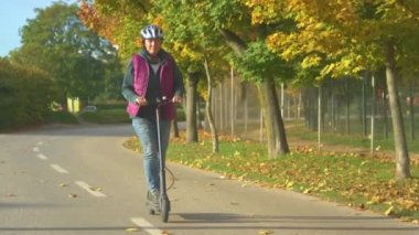 Büyük hanım, güzel bir sonbahar gününde elektrikli scooter sürmekten zevk alıyor. Yaşlı kadın, modern çevre dostu ulaşım yöntemlerini kullanıyor. Kasabada e-scooter sürmek için güzel bir sonbahar günü..