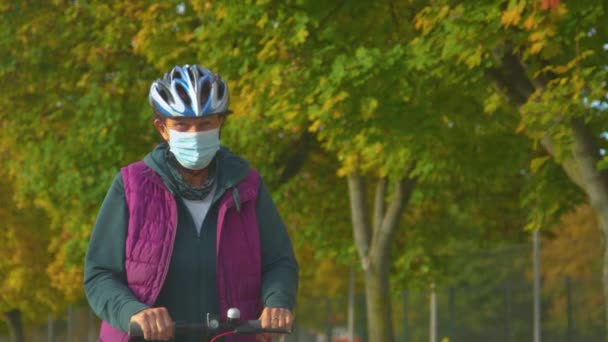 老年女士骑电子摩托车 以避免在电晕时间乘坐公共交通工具 上了年纪的女人带着带着面具的电动车上下班 秋天的天气很好 可以骑着电动车在城里转悠 — 图库视频影像
